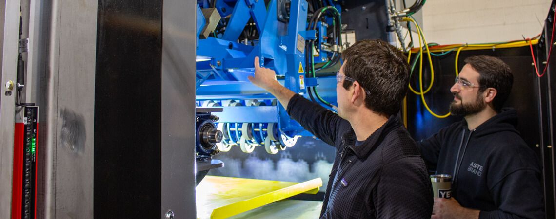 man points to blue machine while co-worker looks at where he's pointing