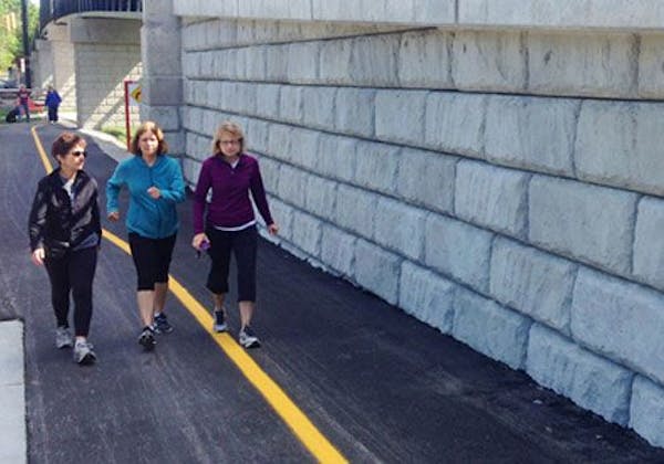Three woman walk on a paved trail adjacent to a retaining wall