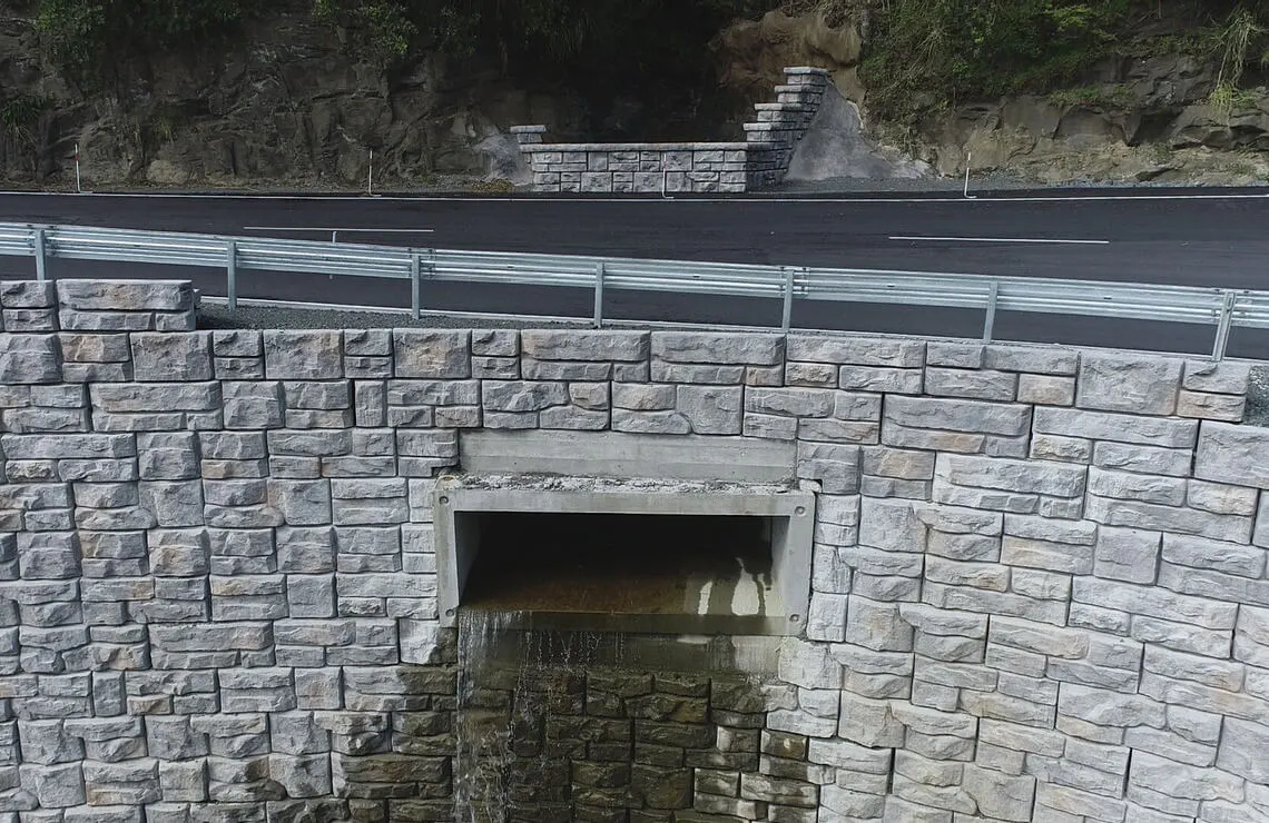 Drainage outlet built into a Ledgestone-textured Redi-Rock retaining wall below a newly paved New Zealand roadway.