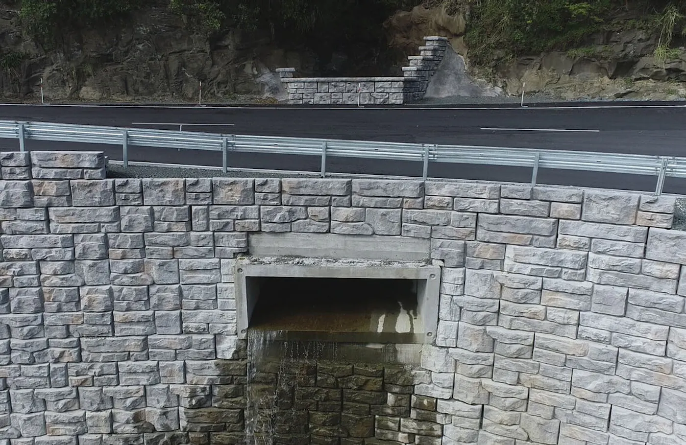 Drainage outlet built into a Ledgestone-textured Redi-Rock retaining wall below a newly paved New Zealand roadway.