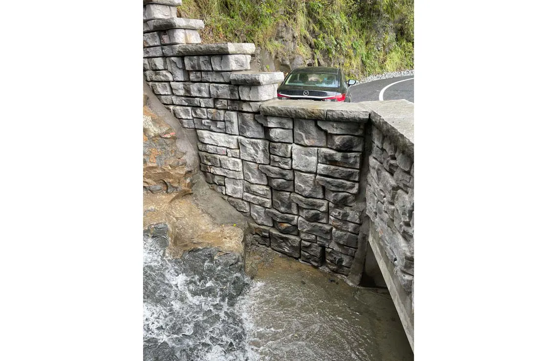 Ledgestone-textured Redi-Rock walls support a narrow, curved New Zealand roadway above a flowing stream.