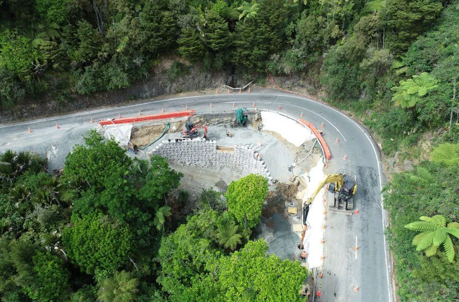 Aerial view of crews constructing a Redi-Rock hybrid retaining wall along a curved, forested New Zealand roadway.