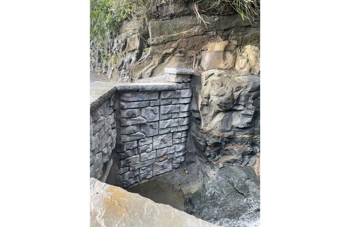 Ledgestone-textured Redi-Rock wall built against exposed rock along a New Zealand roadway.