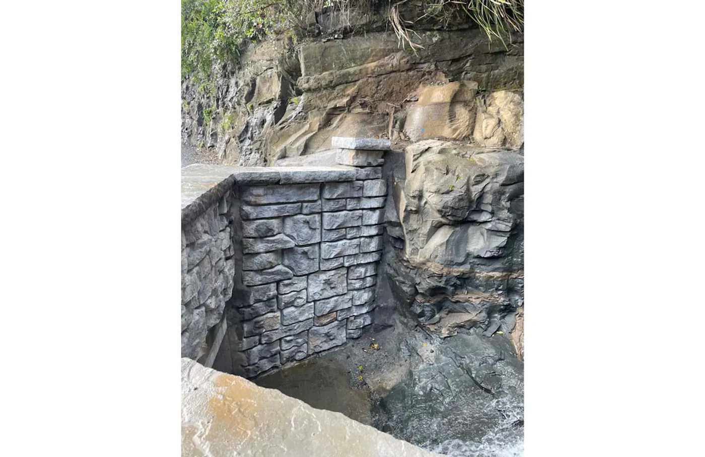 Ledgestone-textured Redi-Rock wall built against exposed rock along a New Zealand roadway.