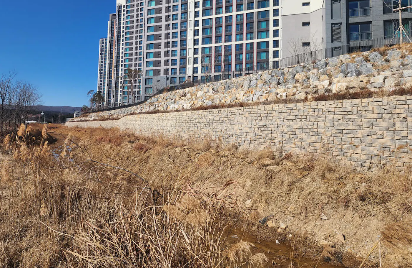 image of redi-rock ledgestone wall with ditch in front and apartments in background
