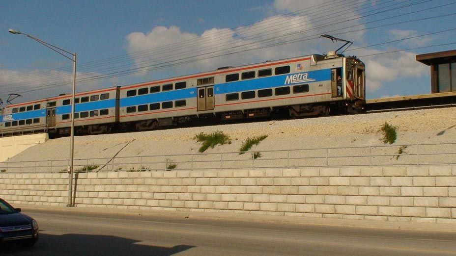 A Metra commuter train goes by with a Limestone retaining wall providing support below