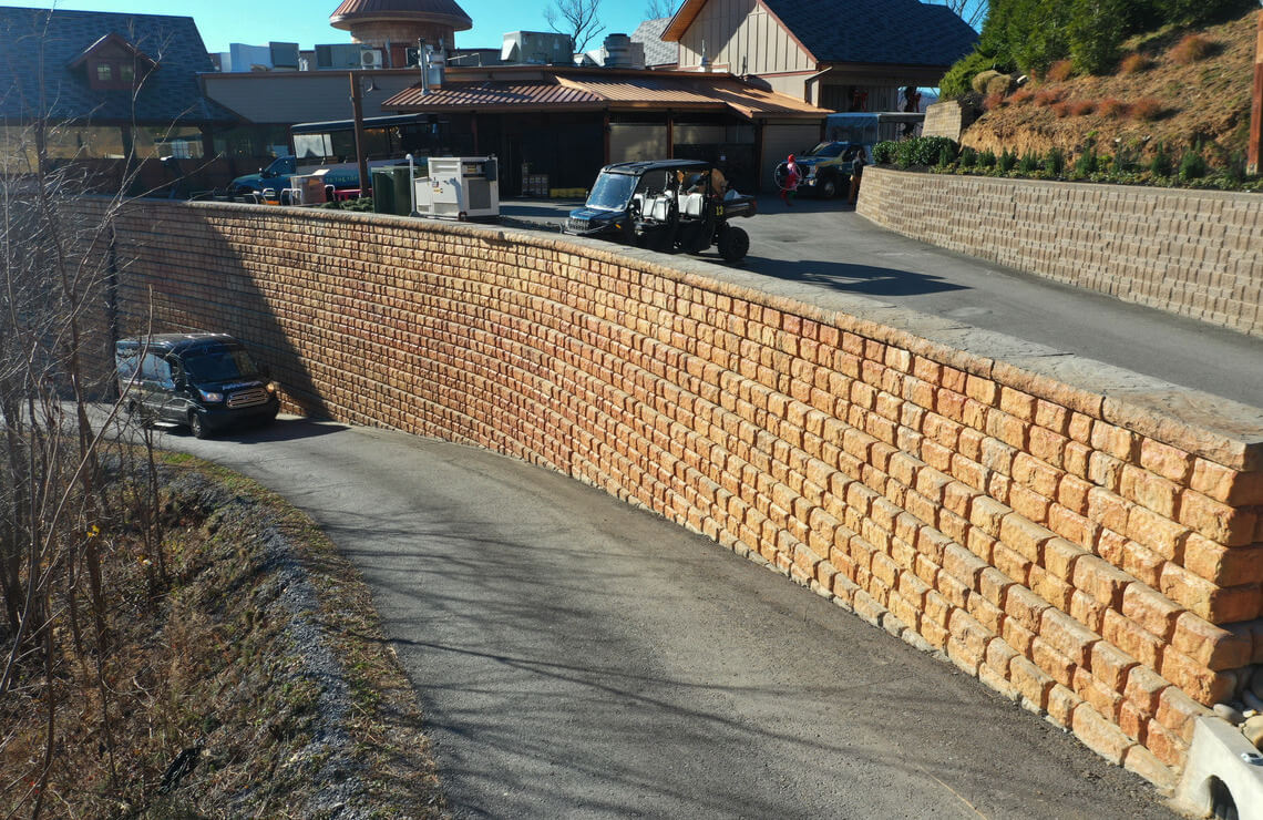 image of color stained redi-rock Cobblestone retaining wall next to road and building