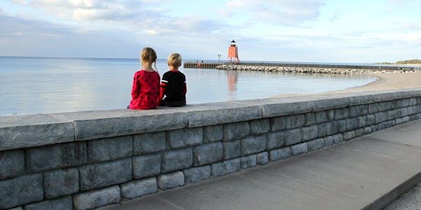 Two kids sit on a Cobblestone texture seat wall looking out at lake and lighthouse