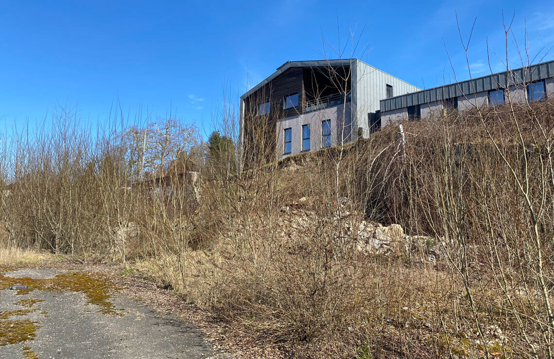 image of unstable dirt hill overgrown with trees and shrubs with building in background