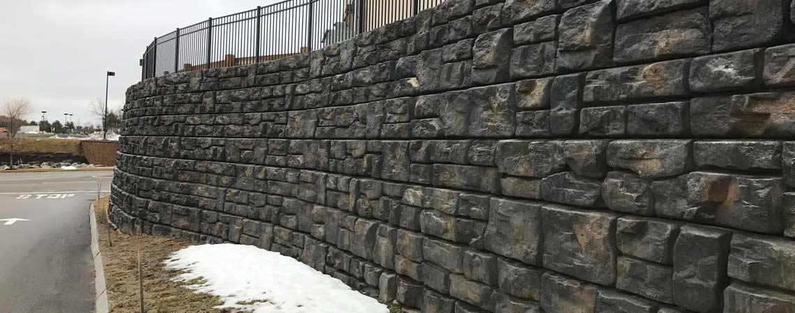 image of redi-rock retaining wall in winter next to road with fence on top of wall
