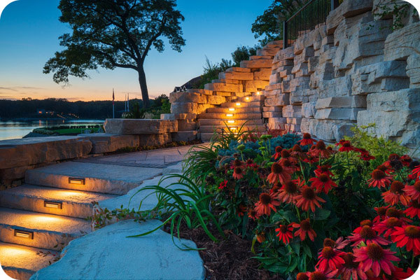 outcropping wall with flowers and lit up stairway overlooking lake at dusk