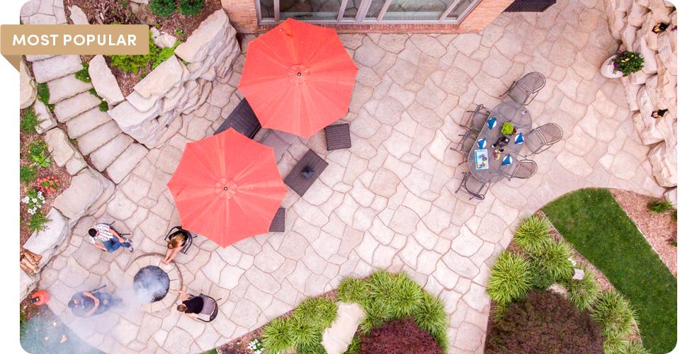 arial view of backyard patio with umbrellas stairway with outcropping walls a firepit and grand flagstone