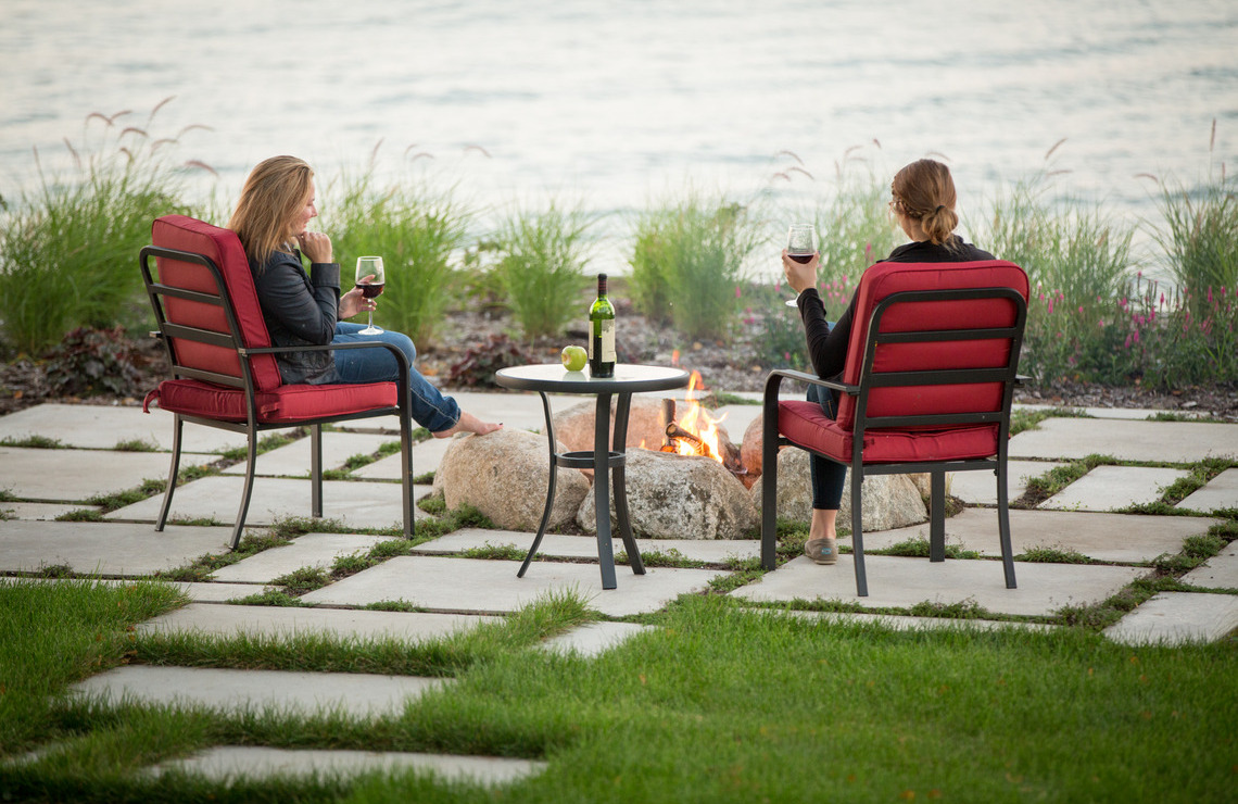 miros slabs with people having wine around fire pit next to water