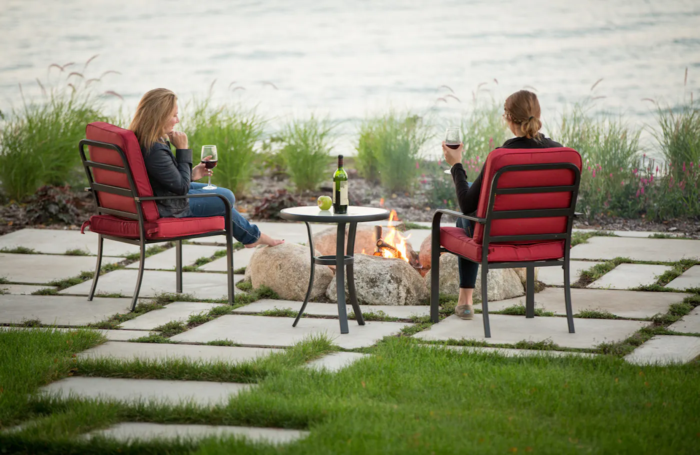miros slabs with people having wine around fire pit next to water