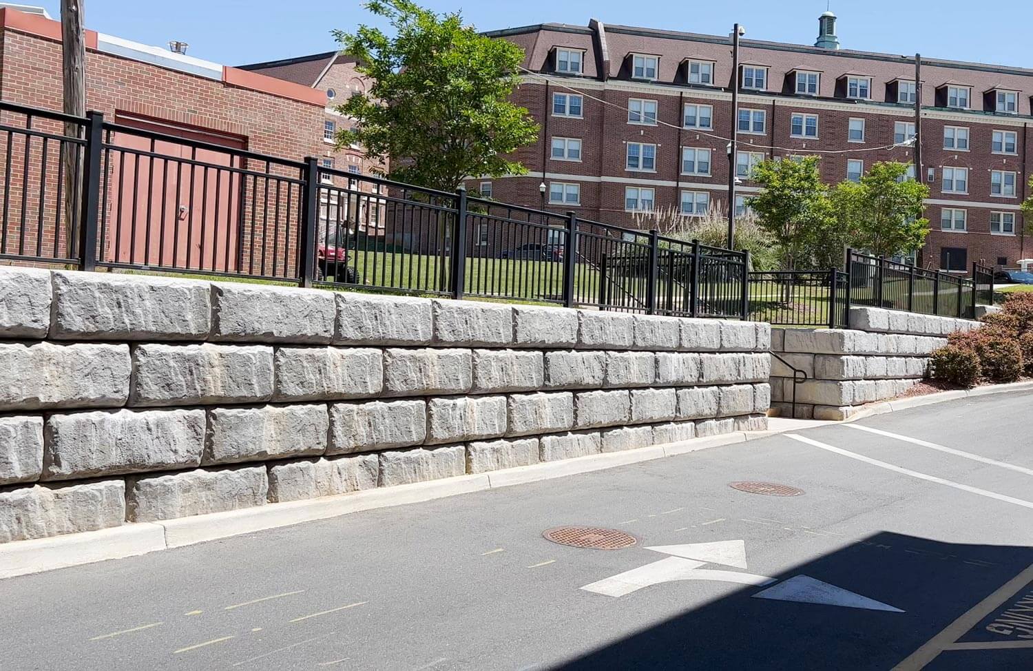 image of limestone textured redi-rock retaining wall with railing on top next to road and university building in background