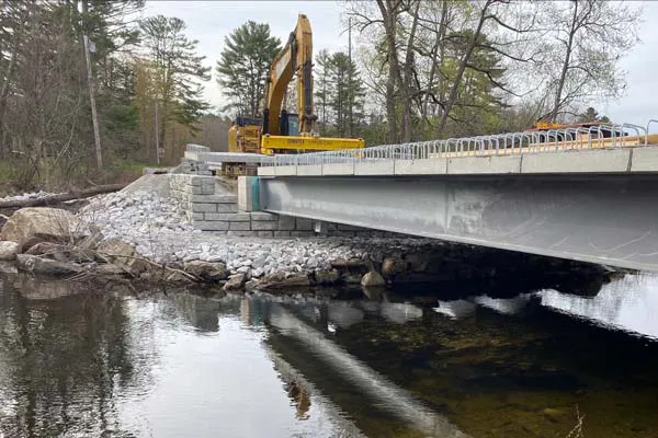 An excavator places the final deck panels on a Velpont precast concrete bridge system in Maine.